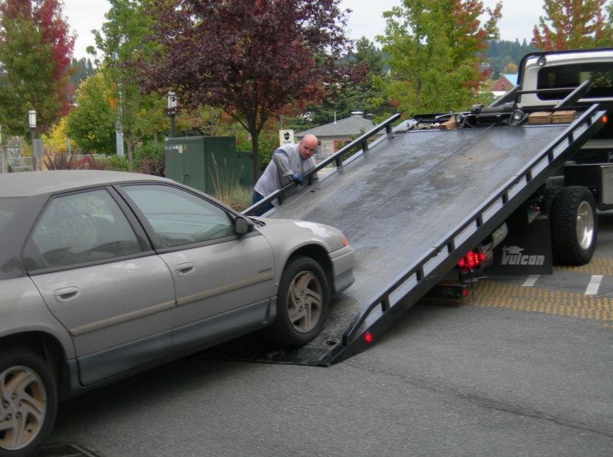 A grey sedan being loaded onto a flatbed tow truck