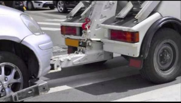 A wheel-lift tow truck towing a silver car